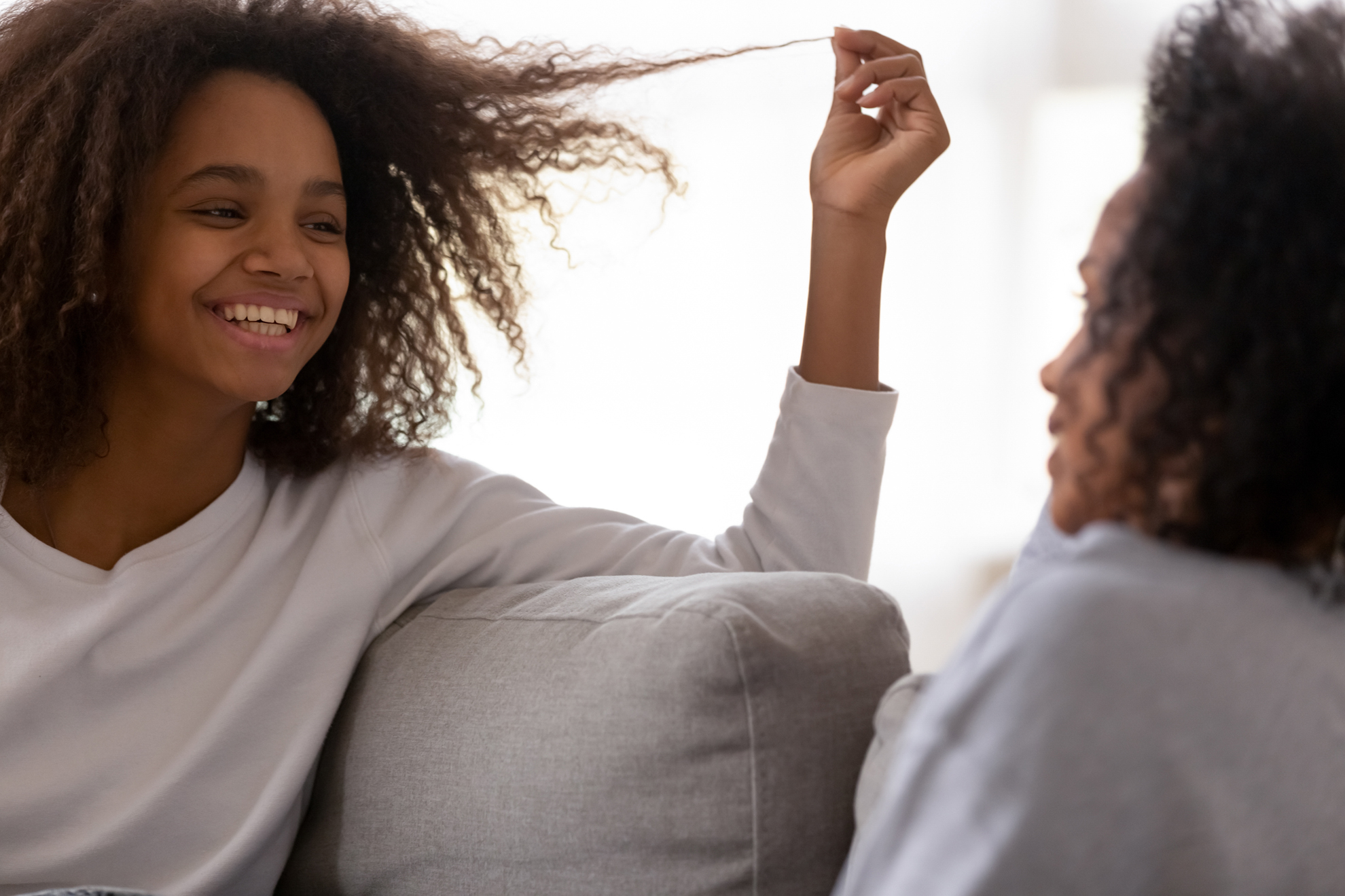 Smiling teenage girl talk with young mom relaxing at home